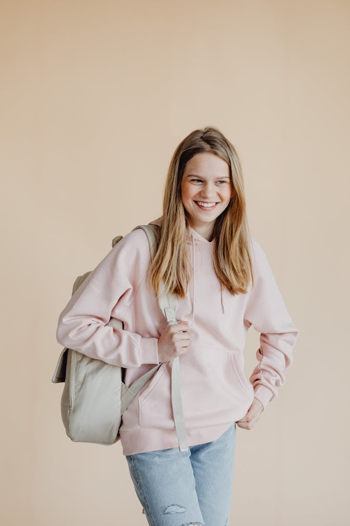 A cheerful teenage girl standing with a backpack ready for school in casual attire.