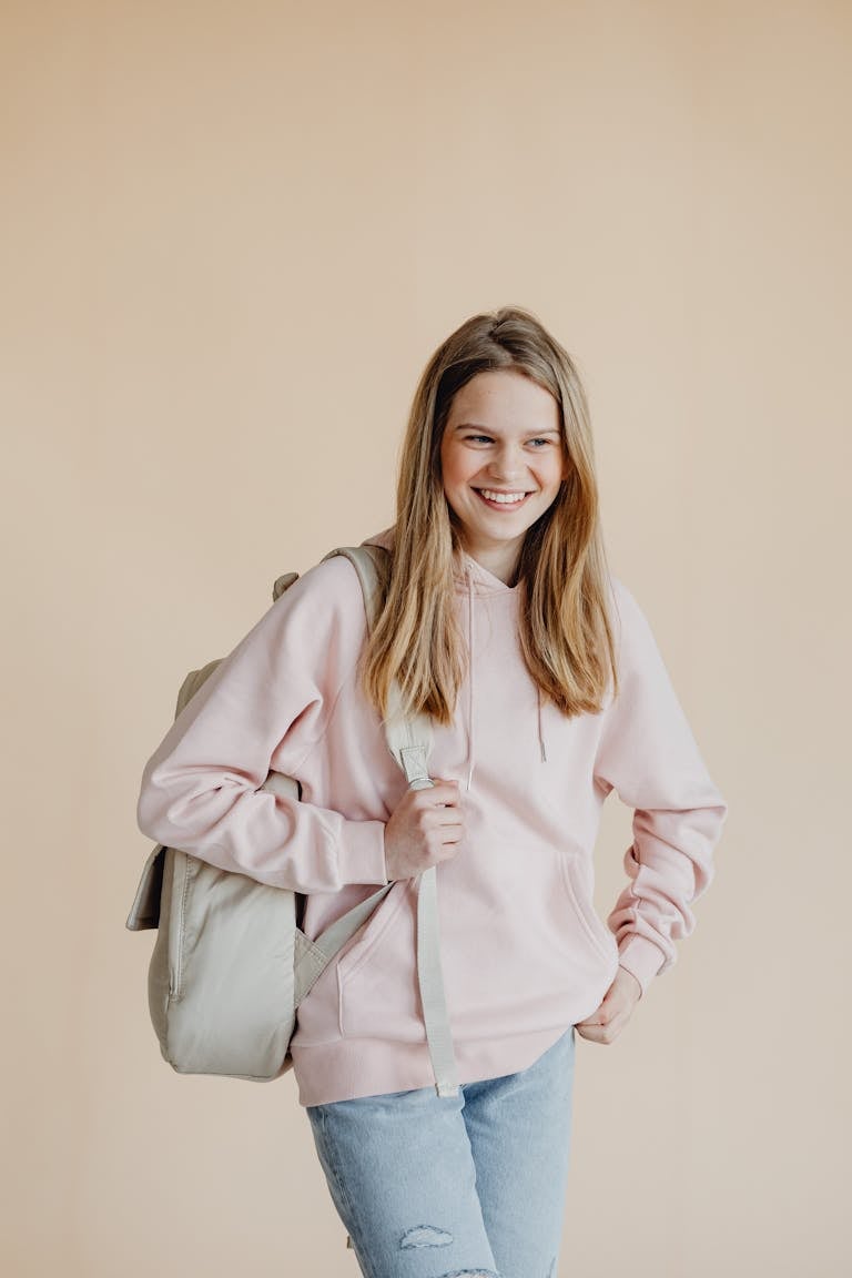 A cheerful teenage girl standing with a backpack ready for school in casual attire.