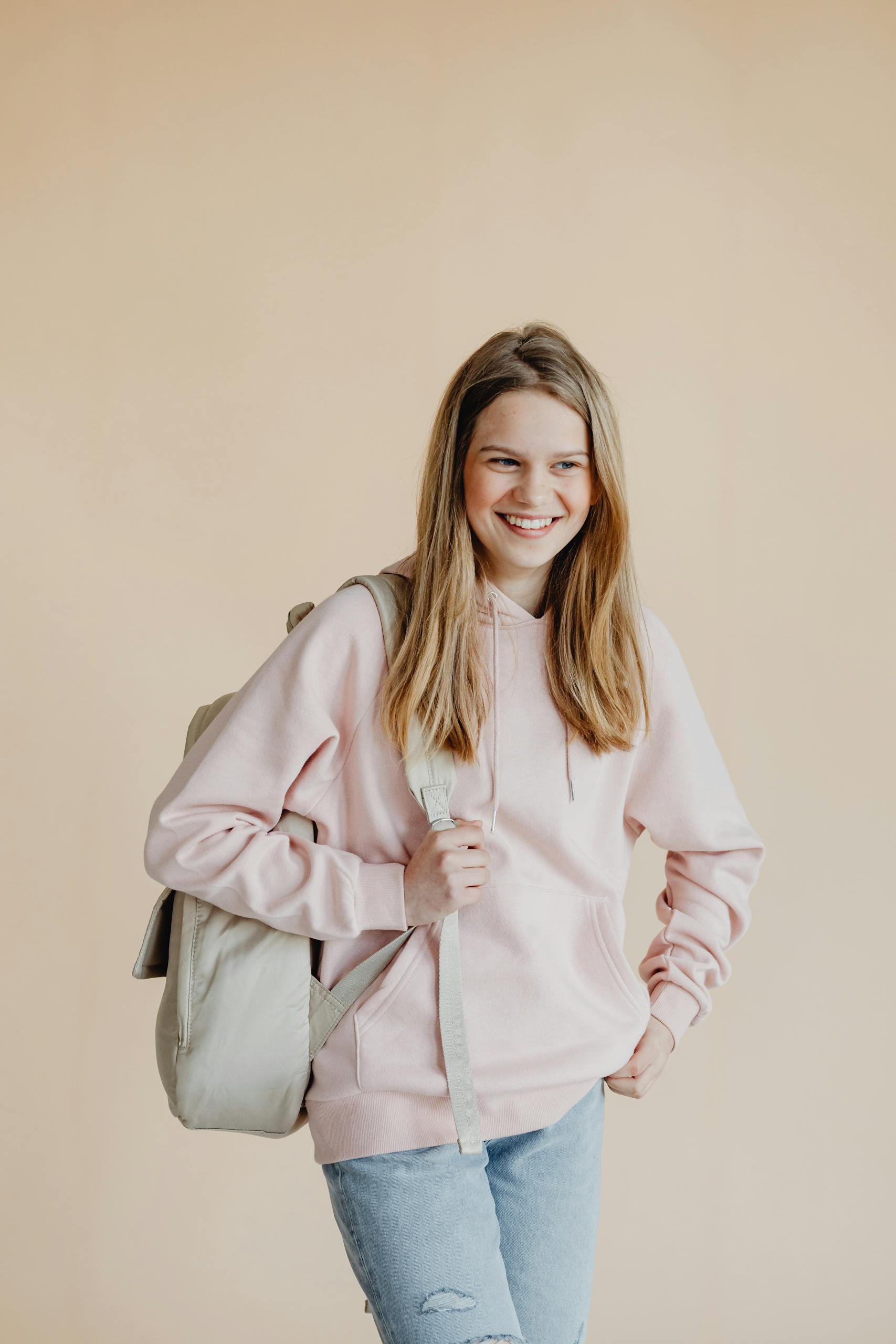 A cheerful teenage girl standing with a backpack ready for school in casual attire.