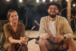 A joyful couple sitting by the campfire enjoying an evening outdoors together.