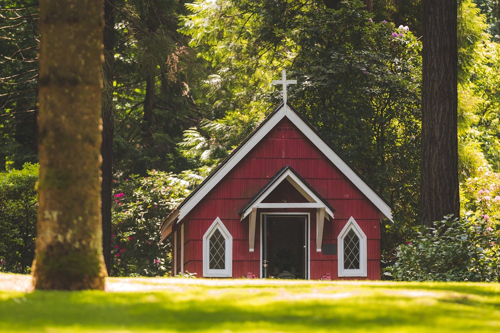 A small red chapel with a white cross nestled in a lush green forest in Portland, Oregon.