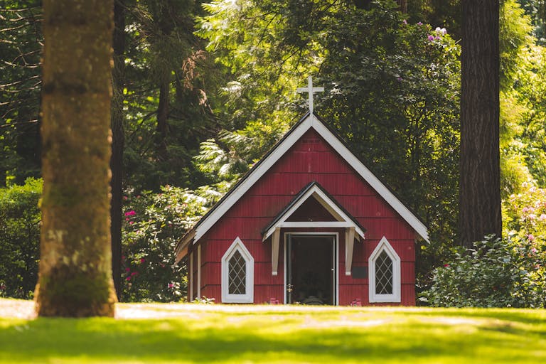 A small red chapel with a white cross nestled in a lush green forest in Portland, Oregon.