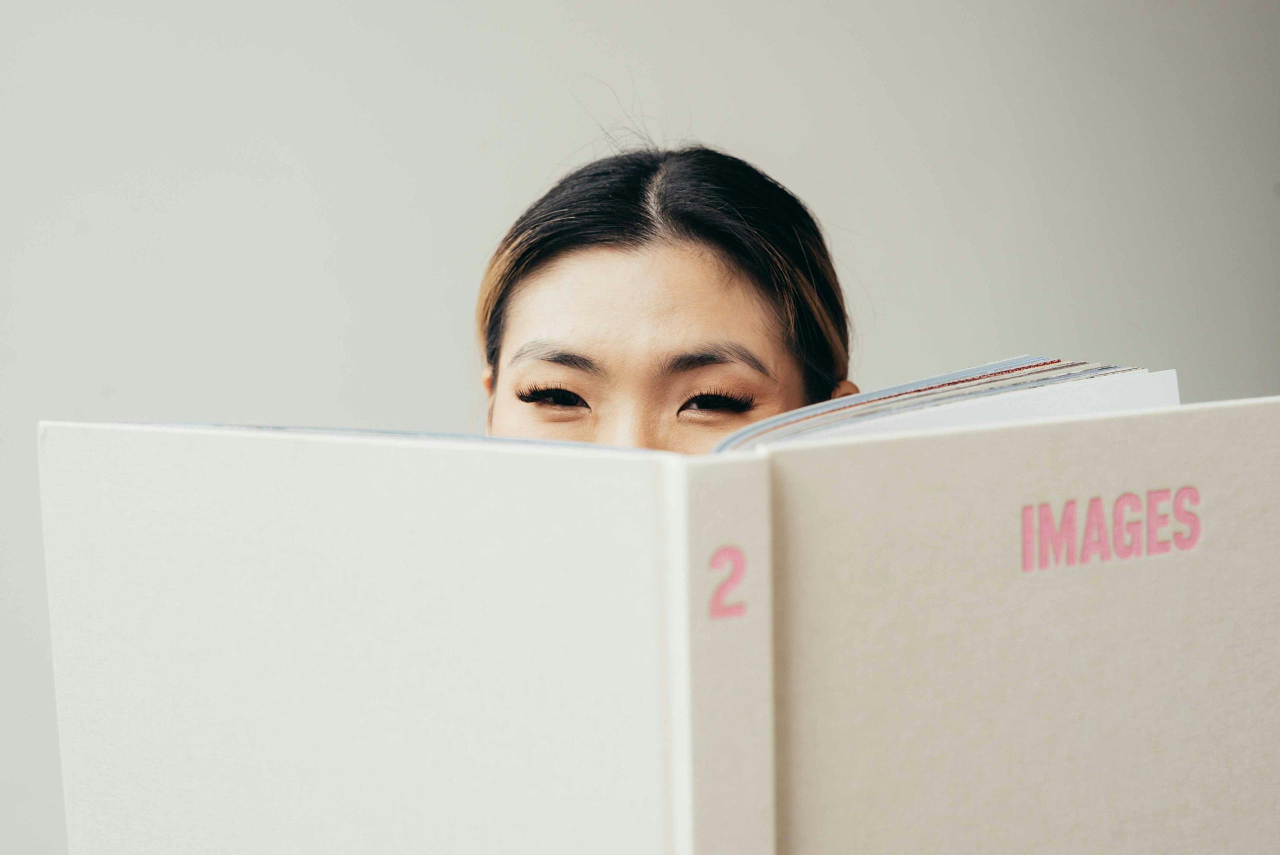 A young woman peeks over a large book, creating a playful and engaging image for stock use.