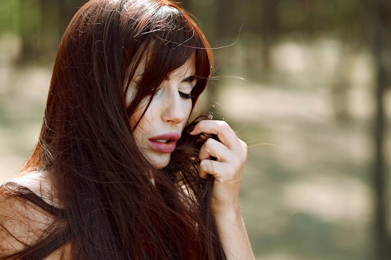 Beautiful woman with long red hair enjoys a tranquil moment in a sun-dappled forest setting.