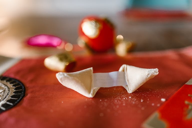 Close-up of a fortune cookie with message on a red tablecloth, symbolizing luck.