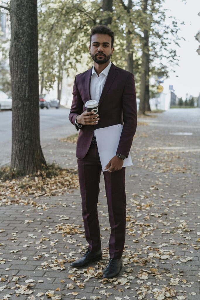 Man in suit holding coffee and document on a leaf-covered street during autumn.