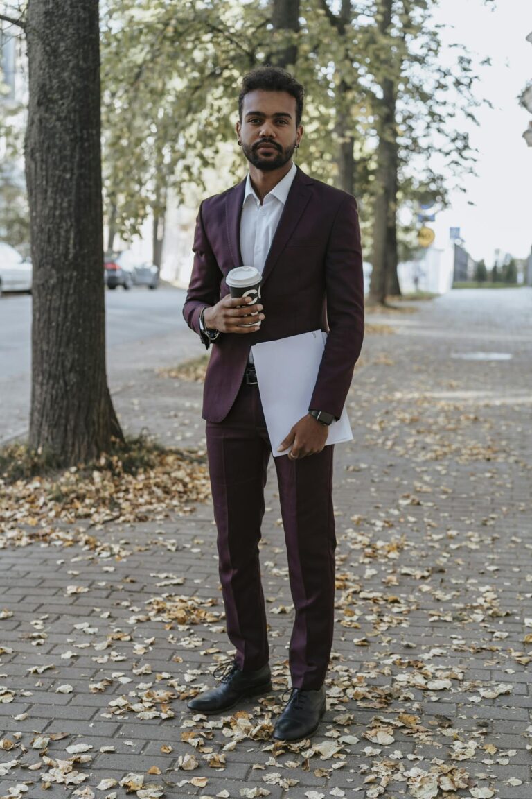 Man in suit holding coffee and document on a leaf-covered street during autumn.