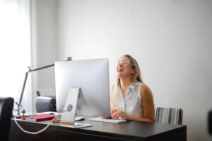 Office scene with a woman laughing while working at a modern desk, showcasing joy and productivity.