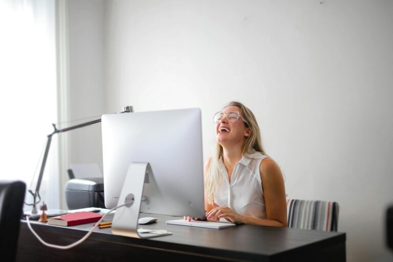 Office scene with a woman laughing while working at a modern desk, showcasing joy and productivity.