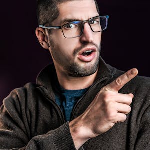 Portrait of a surprised man with eyeglasses pointing, dark background.