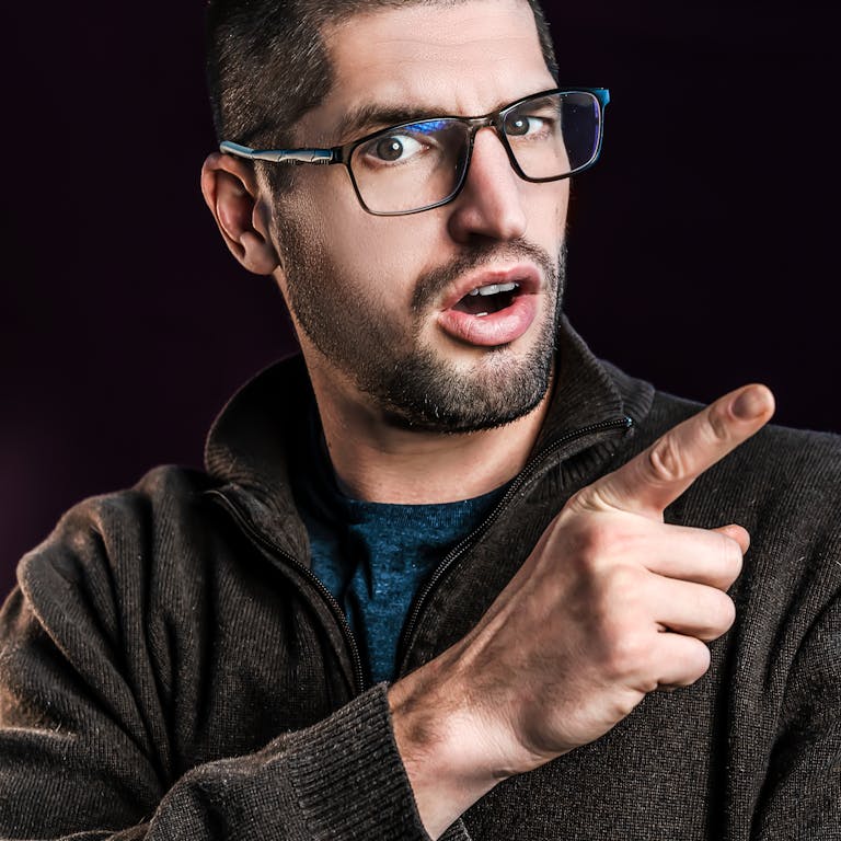 Portrait of a surprised man with eyeglasses pointing, dark background.