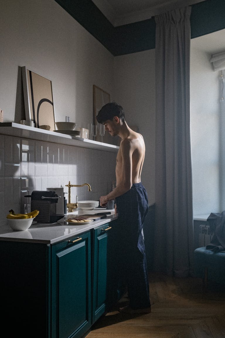 Shirtless man preparing breakfast in a minimalist kitchen, emphasizing a serene morning routine.