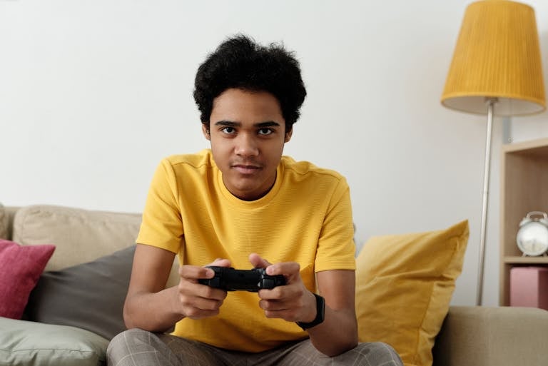 Teen playing video games on a couch, wearing a yellow shirt, indoors.