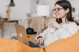 Woman enjoying a cozy moment with a laptop and coffee in a modern interior setting.
