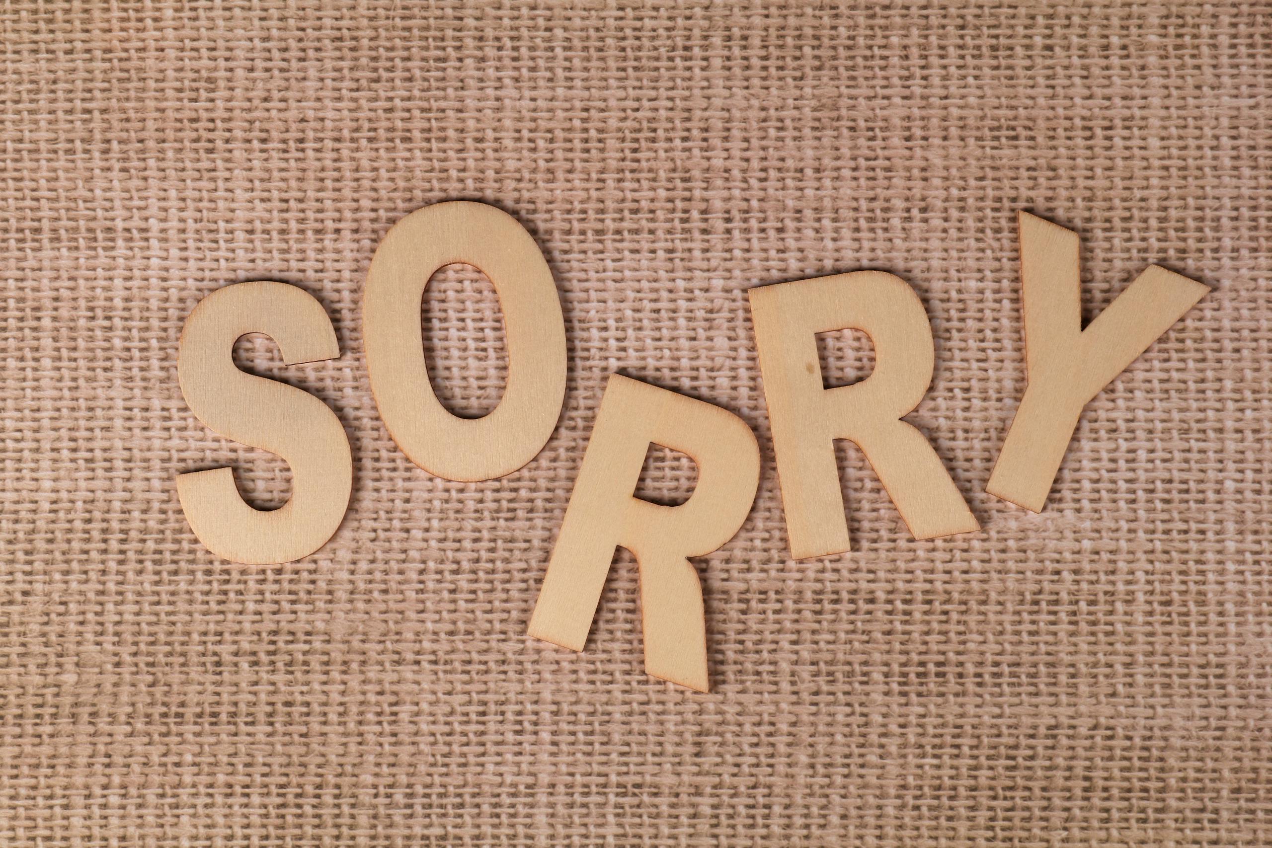 Wooden letters forming 'SORRY' on a burlap surface, offering a rustic apology vibe.