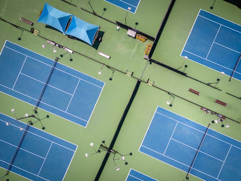 Aerial view of multiple blue tennis courts with striking geometric patterns.