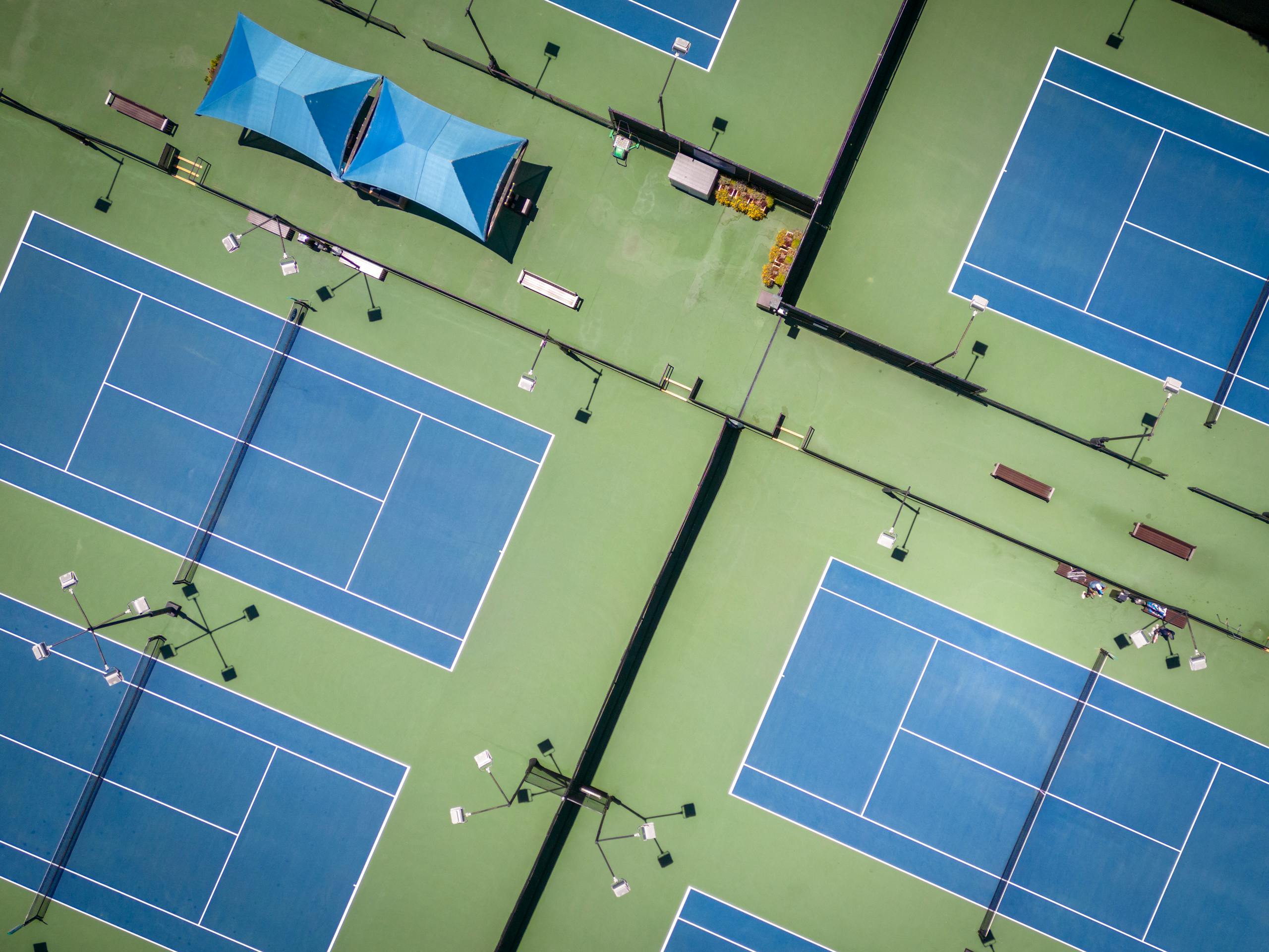 Aerial view of multiple blue tennis courts with striking geometric patterns.