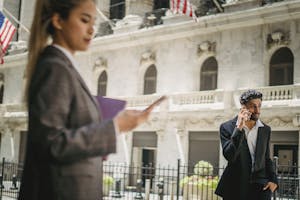 Business professionals in suits using smartphones outside a grand building.