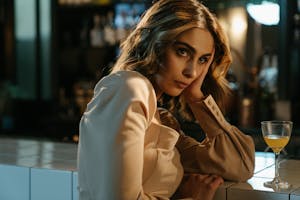 Elegant woman sitting at a bar counter with a cocktail, lost in thought.