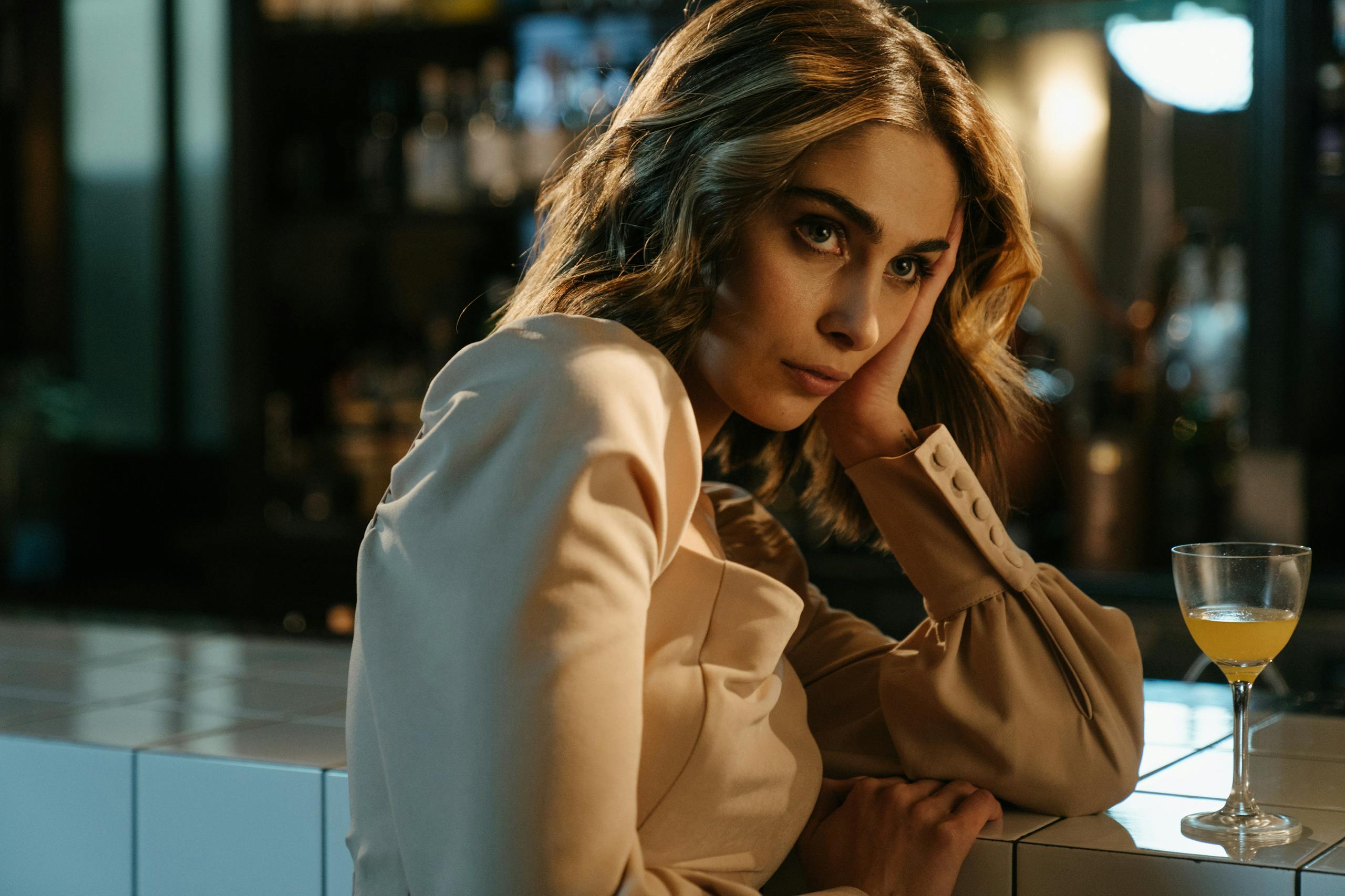 Elegant woman sitting at a bar counter with a cocktail, lost in thought.