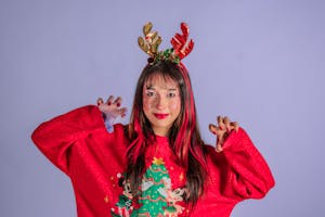 Woman wearing a red Christmas sweater and antler headband, expressing festive joy.