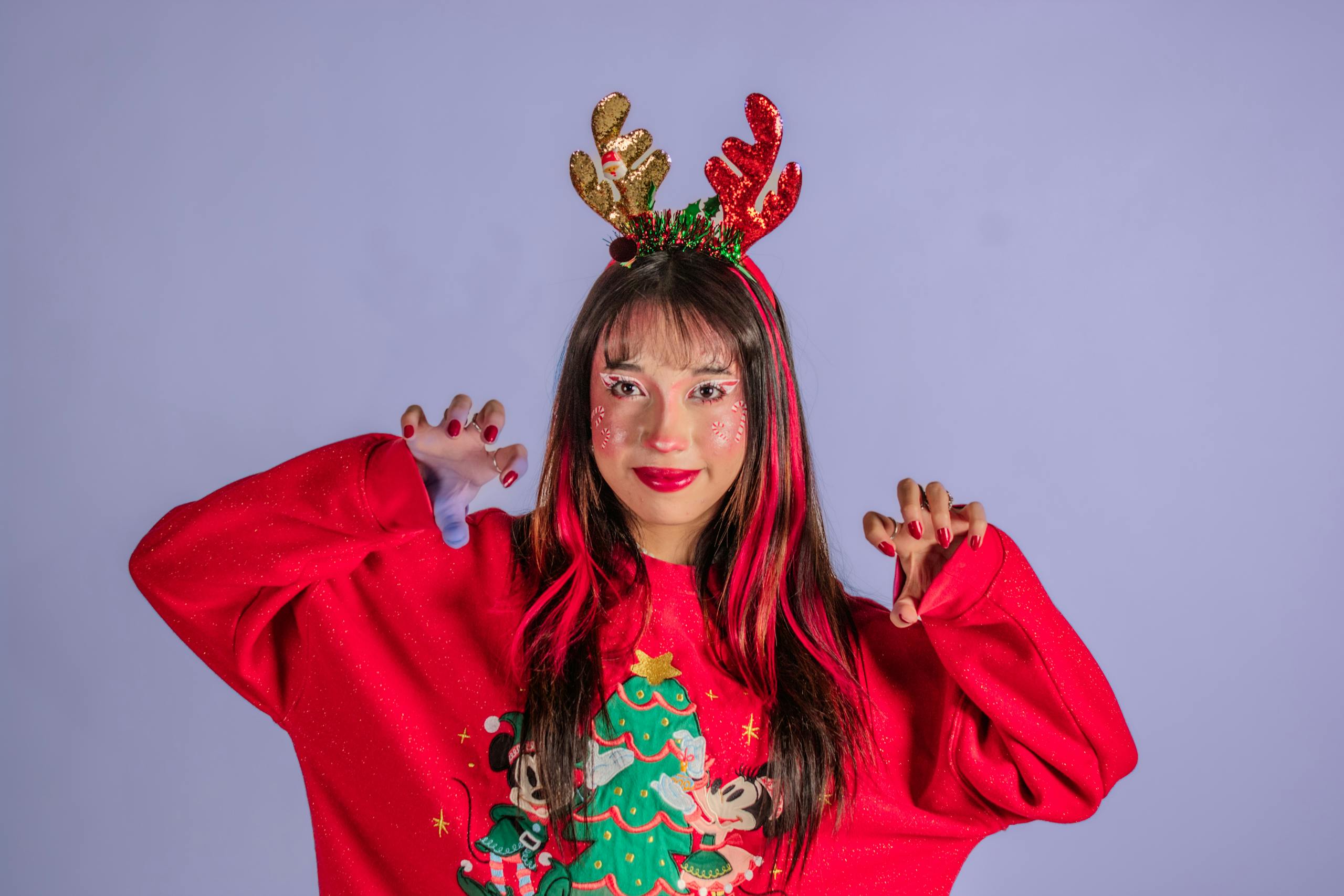 Woman wearing a red Christmas sweater and antler headband, expressing festive joy.