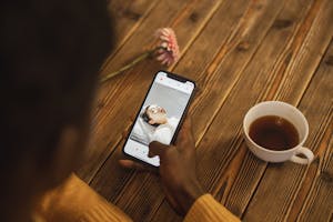 An individual using a dating app on a smartphone with a cup of tea nearby on a wooden table.
