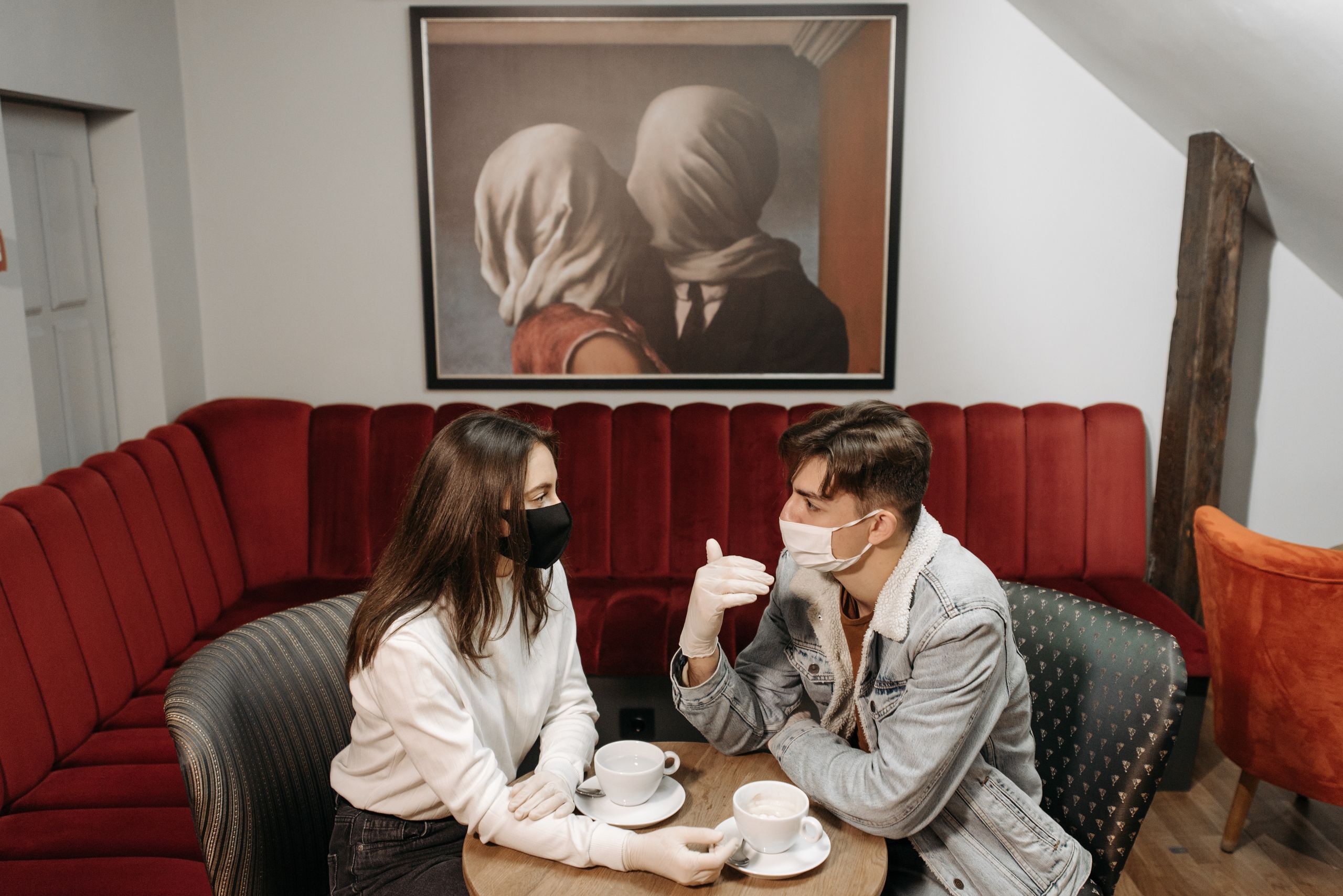 A couple enjoys coffee while wearing masks in a cozy caf&eacute;, highlighting the pandemic's impact.