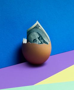 A cracked egg revealing US dollar bill against a vibrant abstract background, symbolizing financial growth.